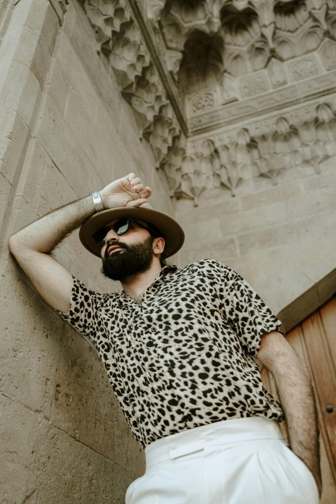 Man wearing a leopard print short sleeve shirt with white trousers and sunglasses for a luxury resort outfit